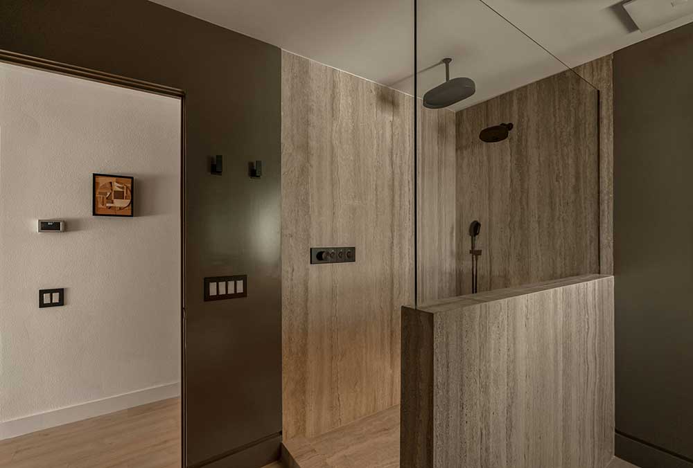 bathroom remodel shower with beige stone walls, black shower fixtures, and a glass partition.