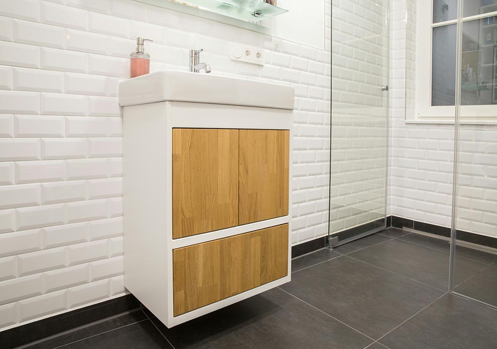 bathroom remodel with white tiled walls, floating vanity with wooden drawers, and glass shower enclosure.