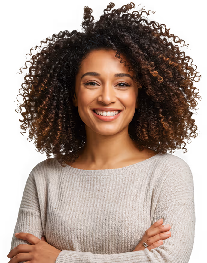 Smiling woman with voluminous curly hair wearing a light gray sweater with arms crossed.