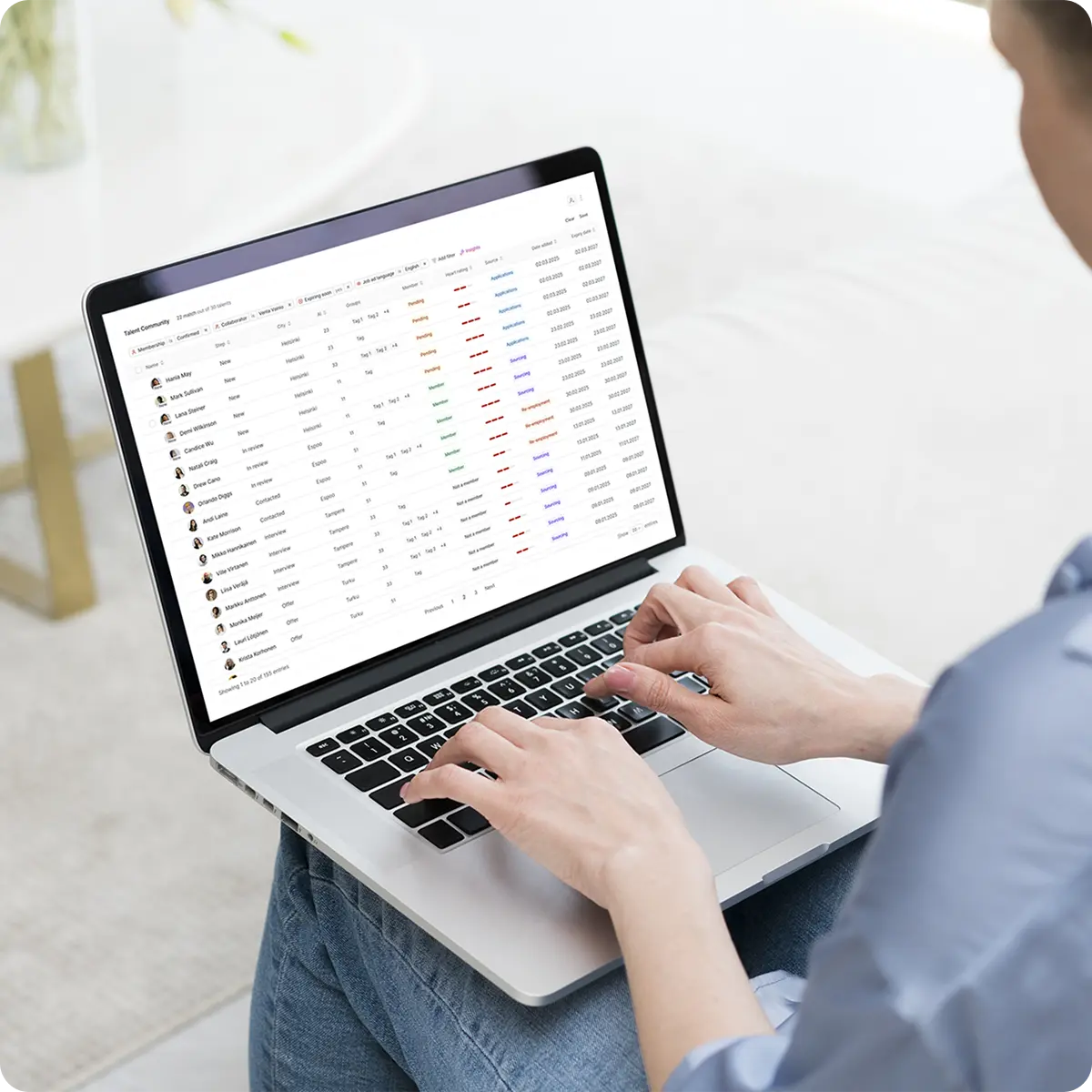 Person typing on a laptop showing a talent management dashboard with candidate names, statuses, and dates.