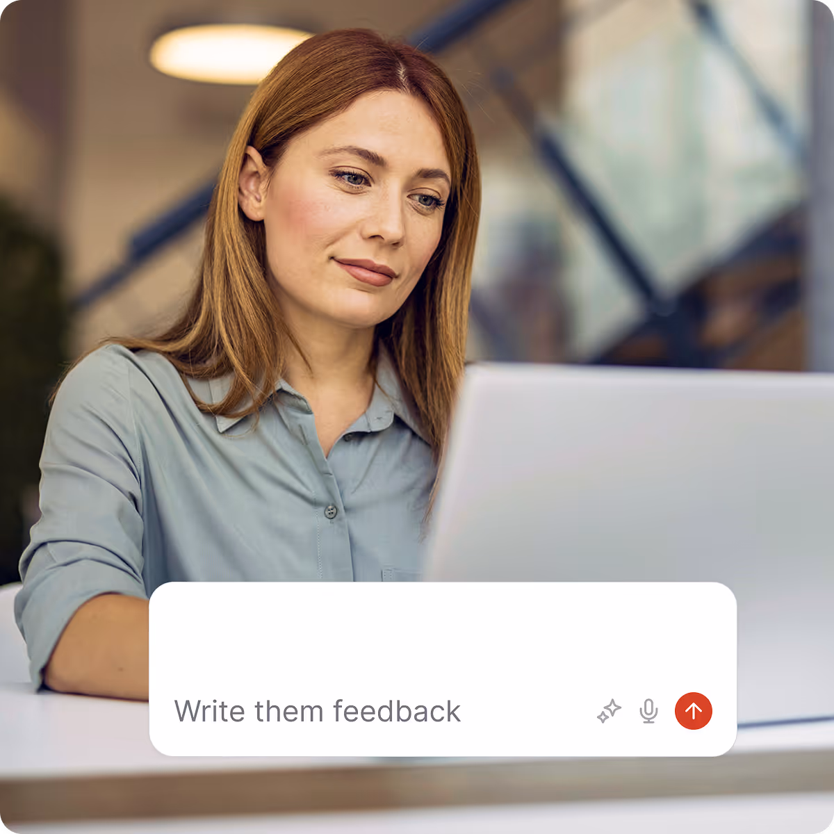 Woman with long brown hair wearing a light blue shirt, sitting and looking at a laptop screen.
