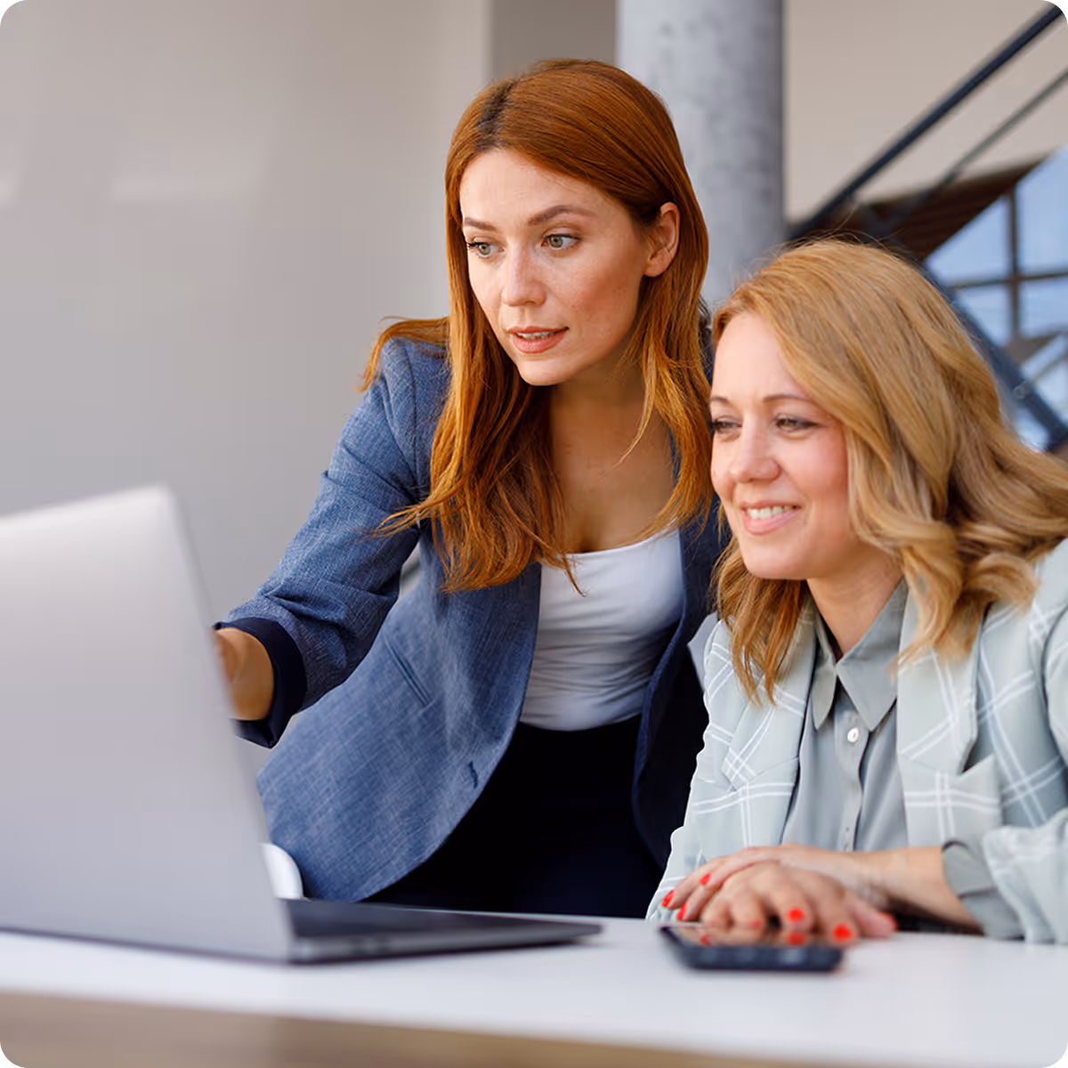 Two professional women looking attentively at a laptop screen in an office setting.