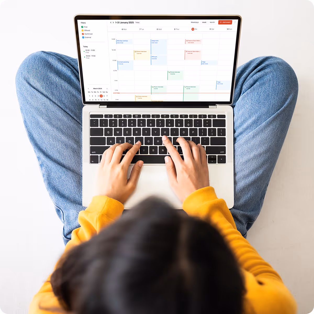 Person in yellow sweater with jeans using a laptop displaying a monthly calendar and schedule.