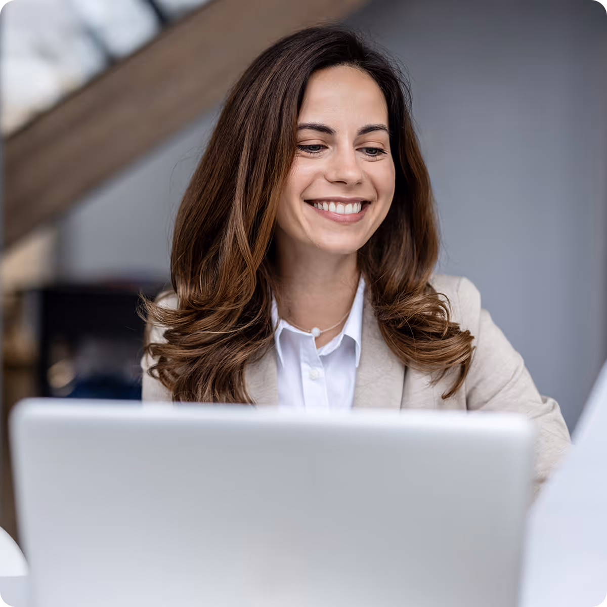 Smiling woman with brown hair looking at a laptop screen in a bright, modern office.