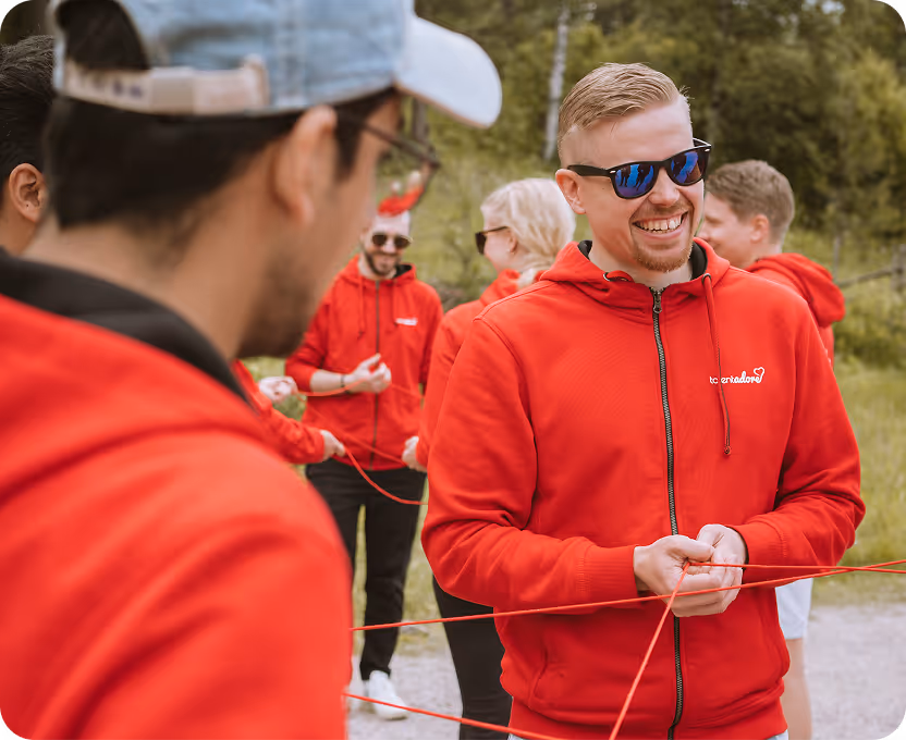 A group of people in red hoodies standing outdoors, smiling and holding red strings as part of a team-building activity.