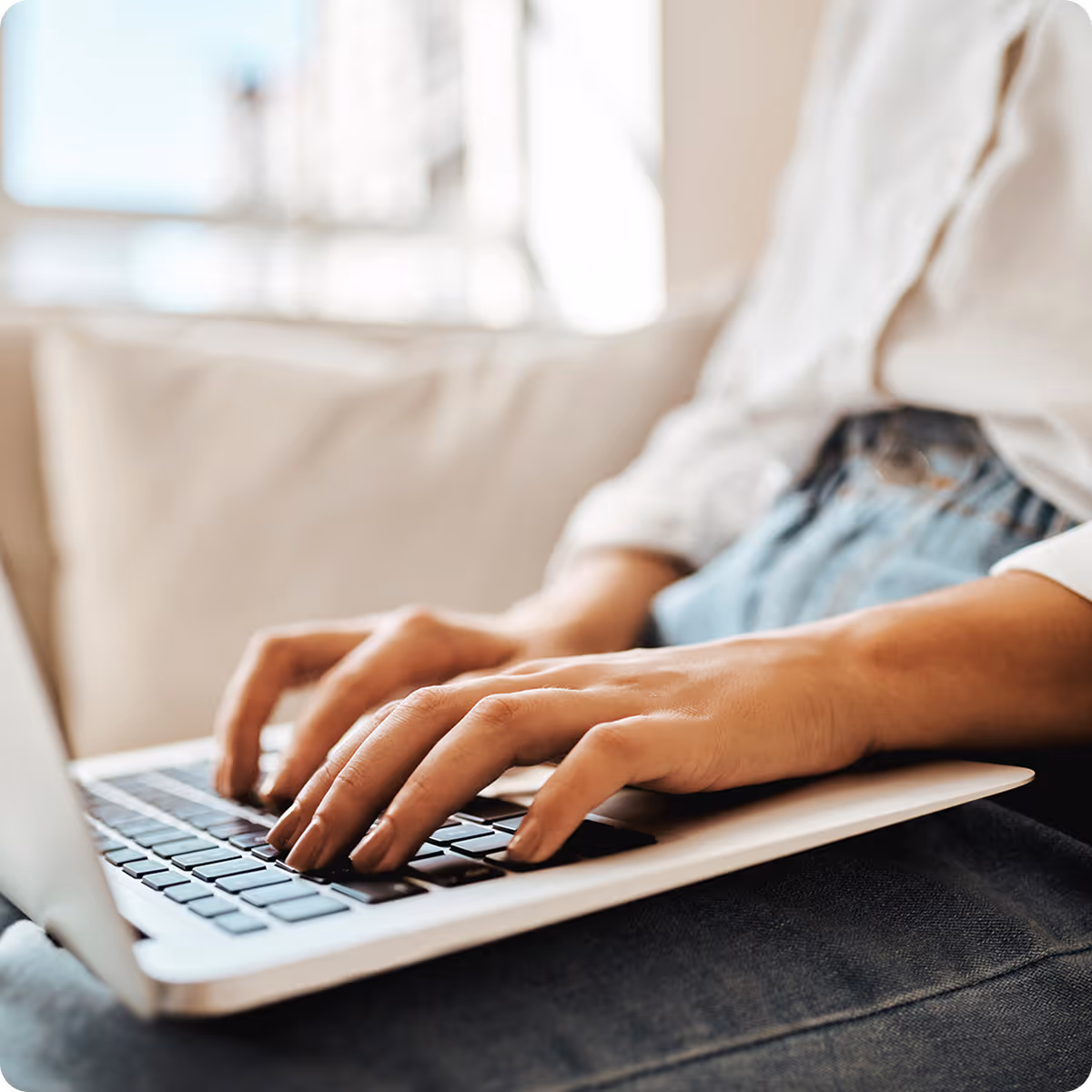 Person typing on a laptop keyboard while sitting on a couch.