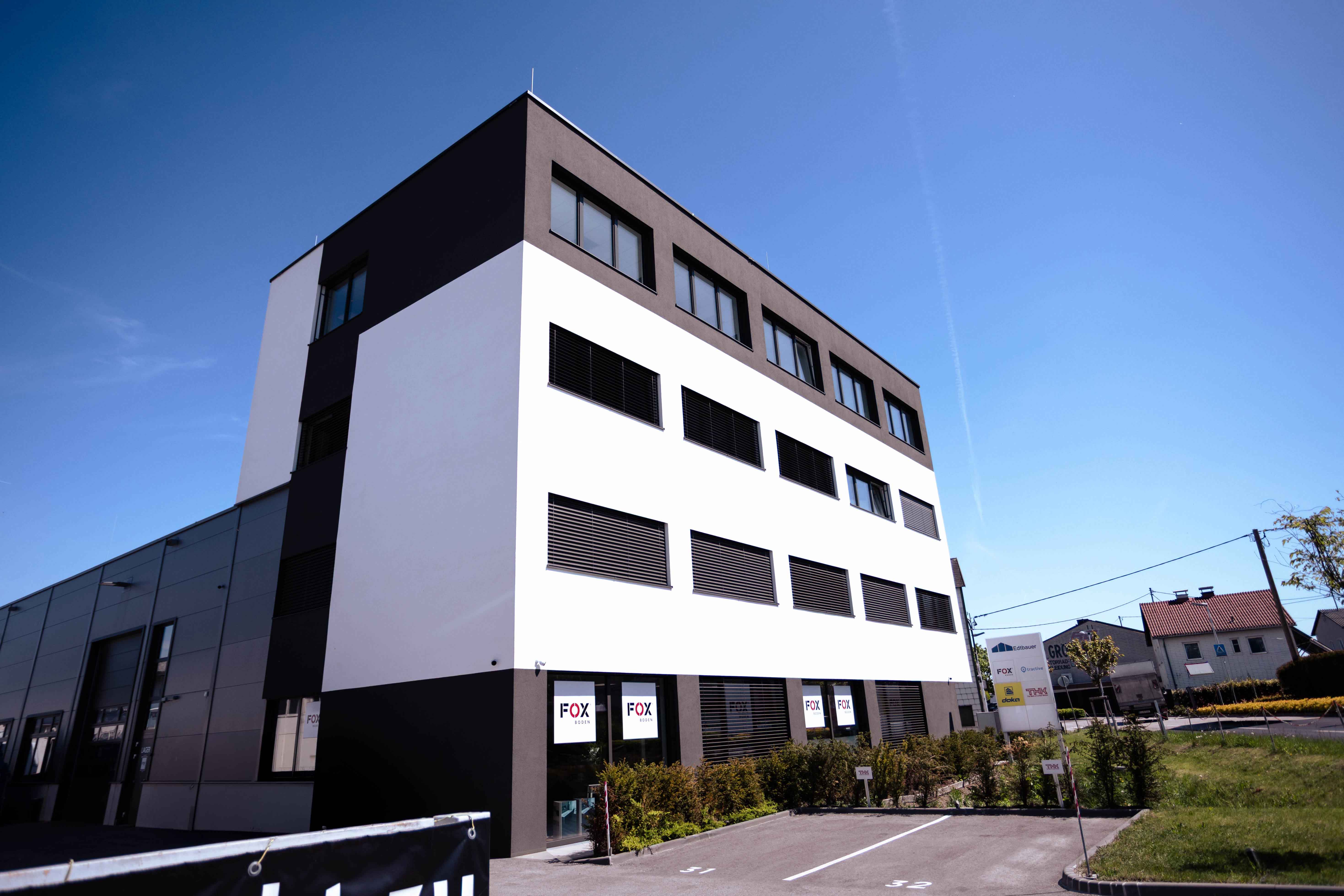Modern dreistöckiges Geschäftsgebäude mit weißen und schwarzen Fassaden bei klarem Himmel.