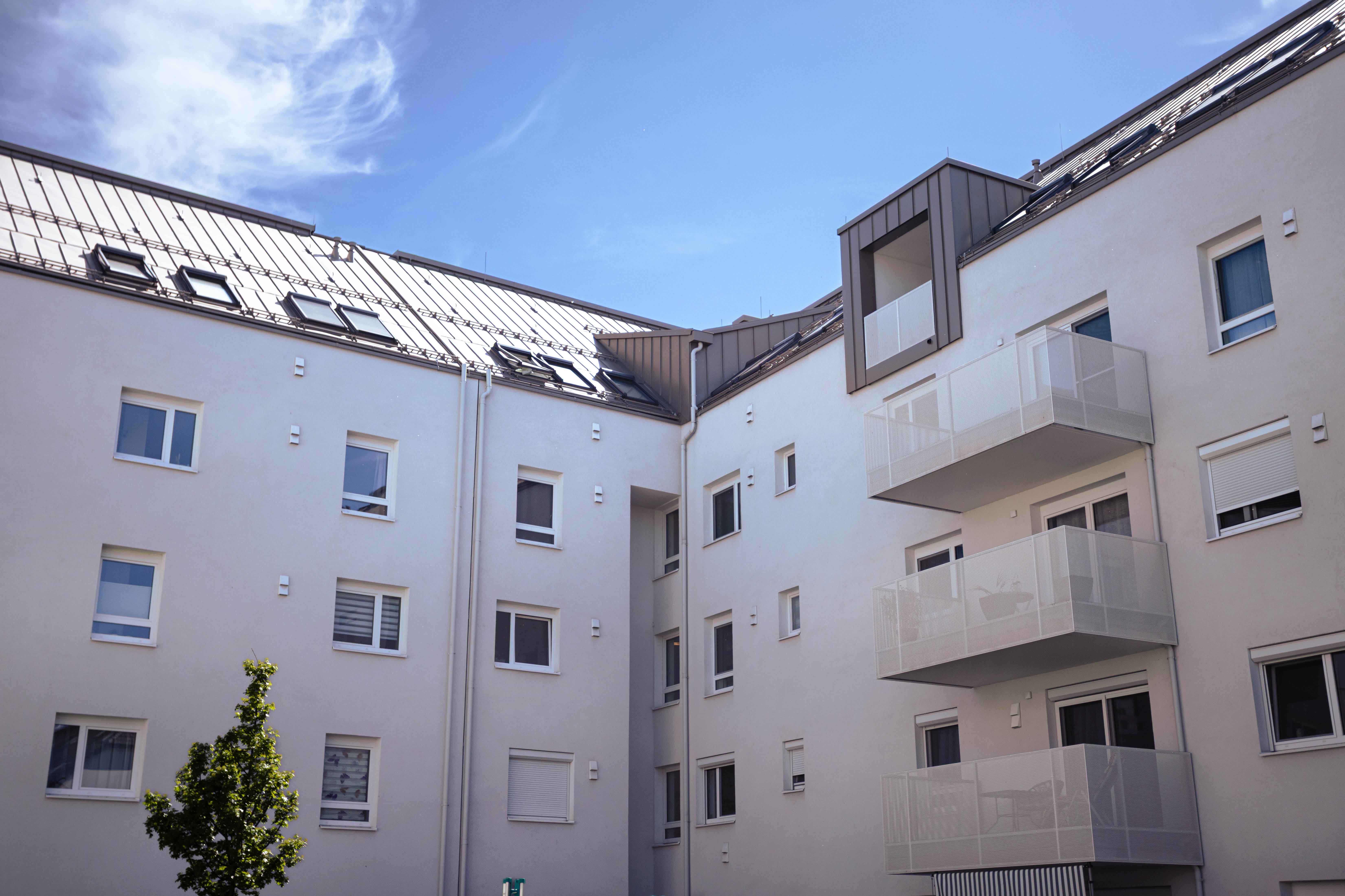 Moderner Wohnblock mit weißen Fassaden, mehreren Fenstern und drei Balkonen unter blauem Himmel.