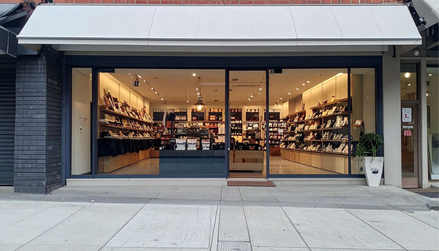 Vue d'une boutique lausannoise soignée, avec vitrine propre et espace de vente bien éclairé. On voit un vendeur souriant en arrière-plan, des sols brillants et une disposition produit impeccable. L'image évoque professionnalisme, propreté et accueil client. Lumière naturelle, ambiance retail haut de gamme.