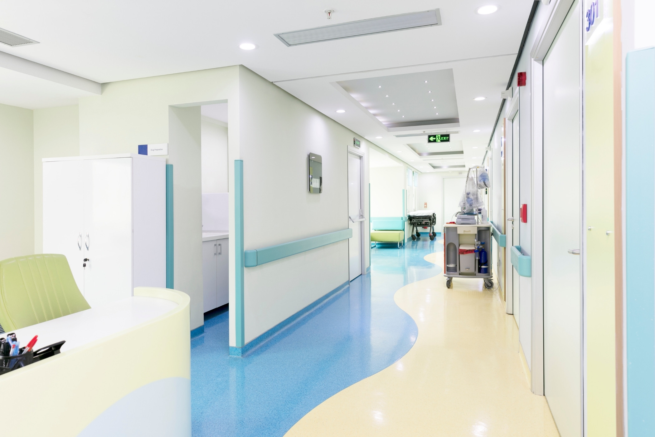 Vue d'un couloir de clinique privée propre et lumineux, sol vinylique brillant, murs blancs, chariot de nettoyage professionnel visible en arrière-plan, ambiance sanitaire rigoureuse.