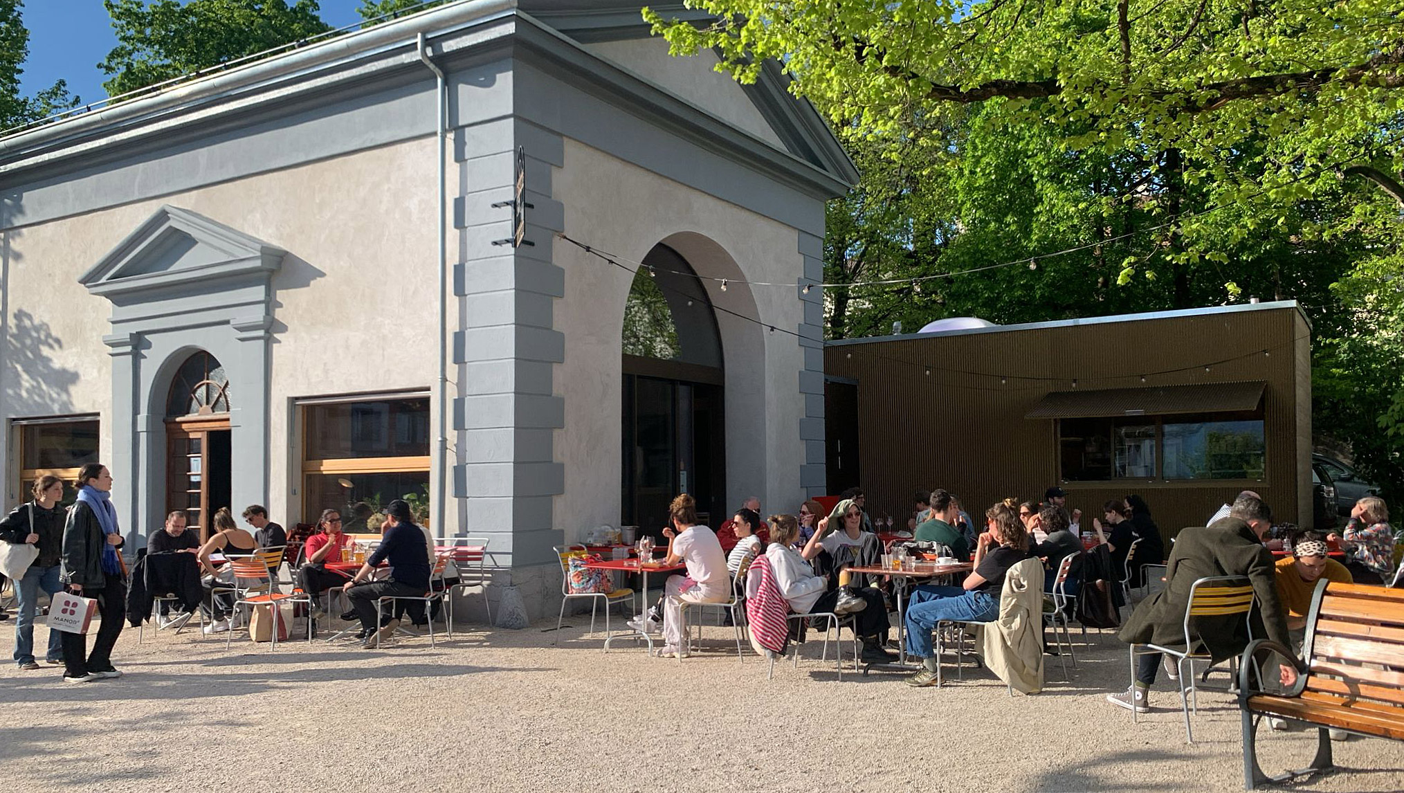 Vue d'une rue commerçante de Montreux en été : terrasses animées, boutiques ouvertes, Lac Léman visible en arrière-plan, vitrine propre et lumineuse au premier plan, ambiance touristique estivale.