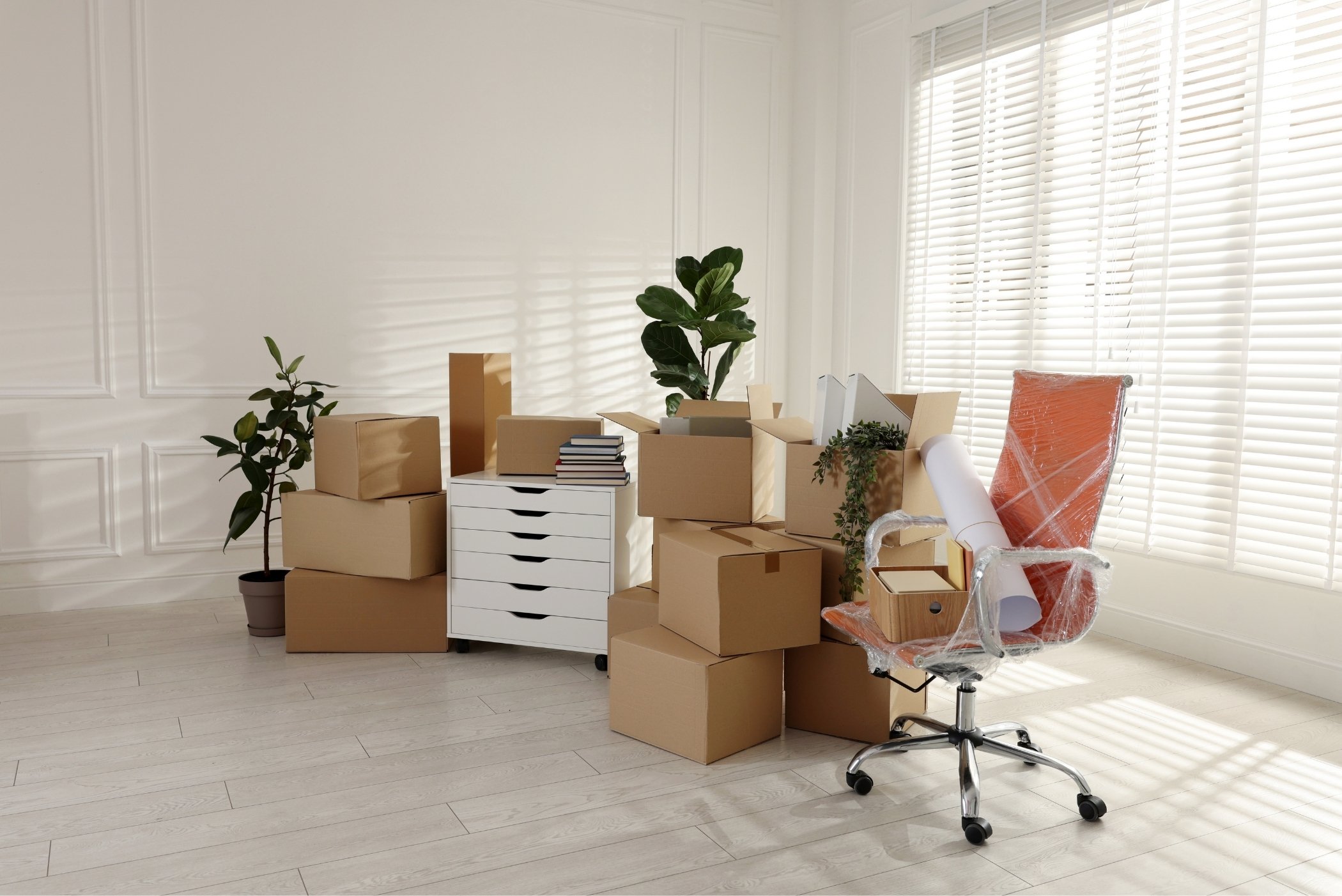 Vue d'un bureau en cours de déménagement à Nyon : cartons empilés, mobilier partiellement démonté, sol propre, lumière naturelle depuis une baie vitrée, ambiance transition professionnelle organisée.