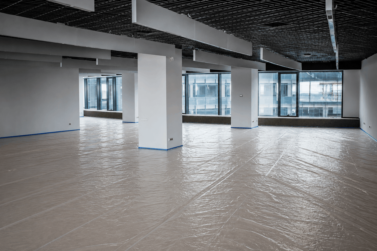 Immeuble neuf en fin de chantier à Lausanne, hall d'entrée avec sol protégé partiellement retiré, lumière naturelle, ambiance de dernière ligne droite avant livraison.