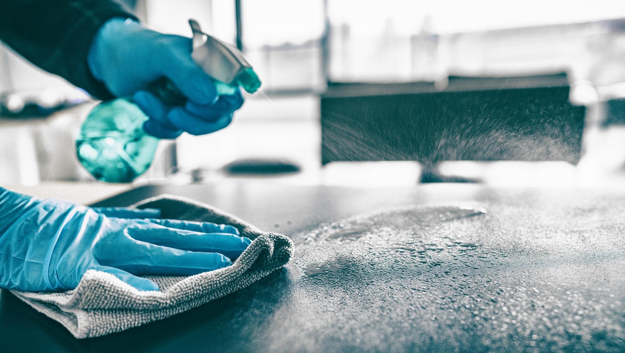 Technicien de nettoyage désinfectant une surface de bureau avec des gants et un spray professionnel, ambiance propre et rigoureuse, lumière naturelle.