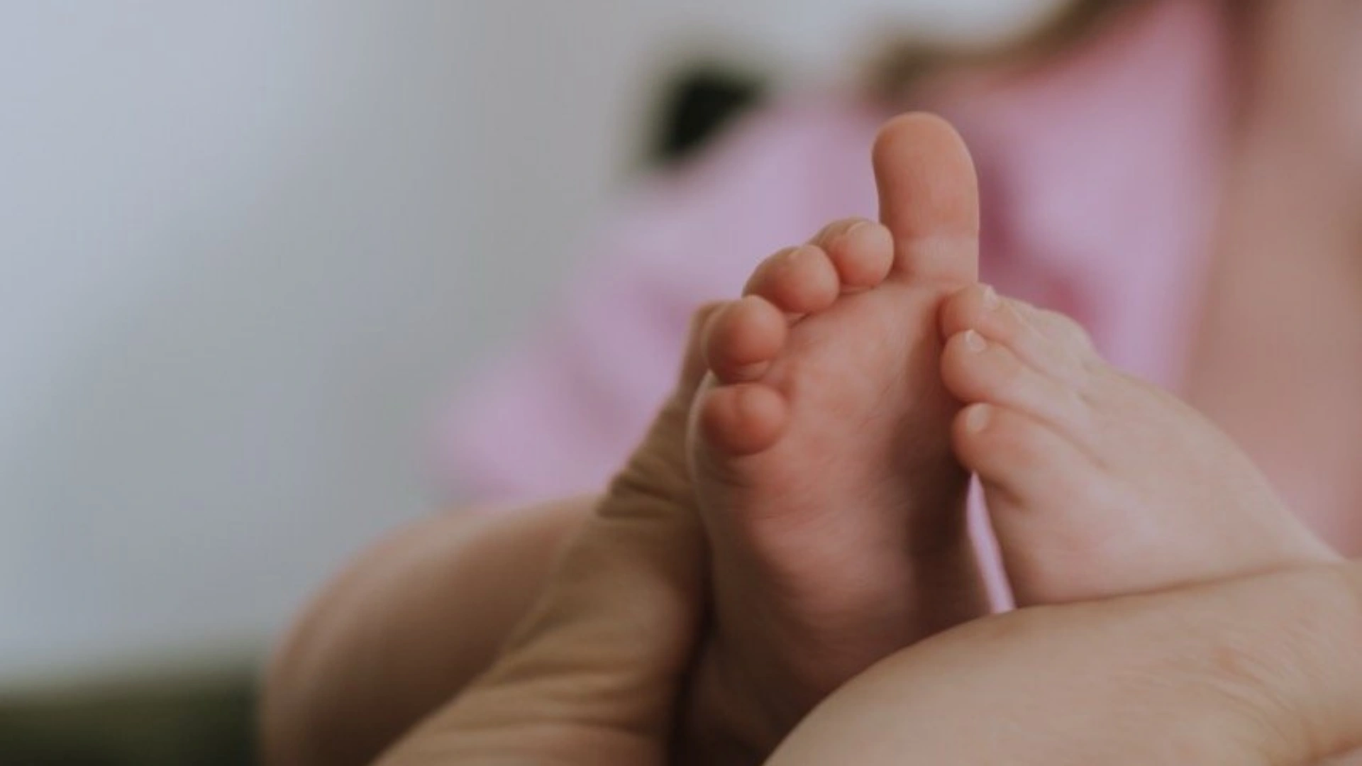 Close-up shot of a midwife's hands gently holding a newborn's tiny feet during checkup