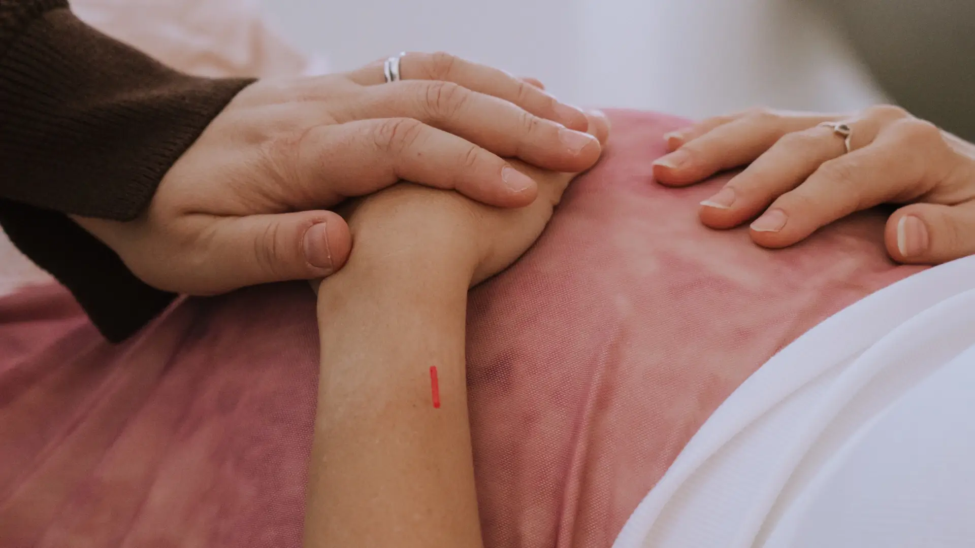 Photo of a midwife's hands performing acuneedling on a client's hand during a prenatal session