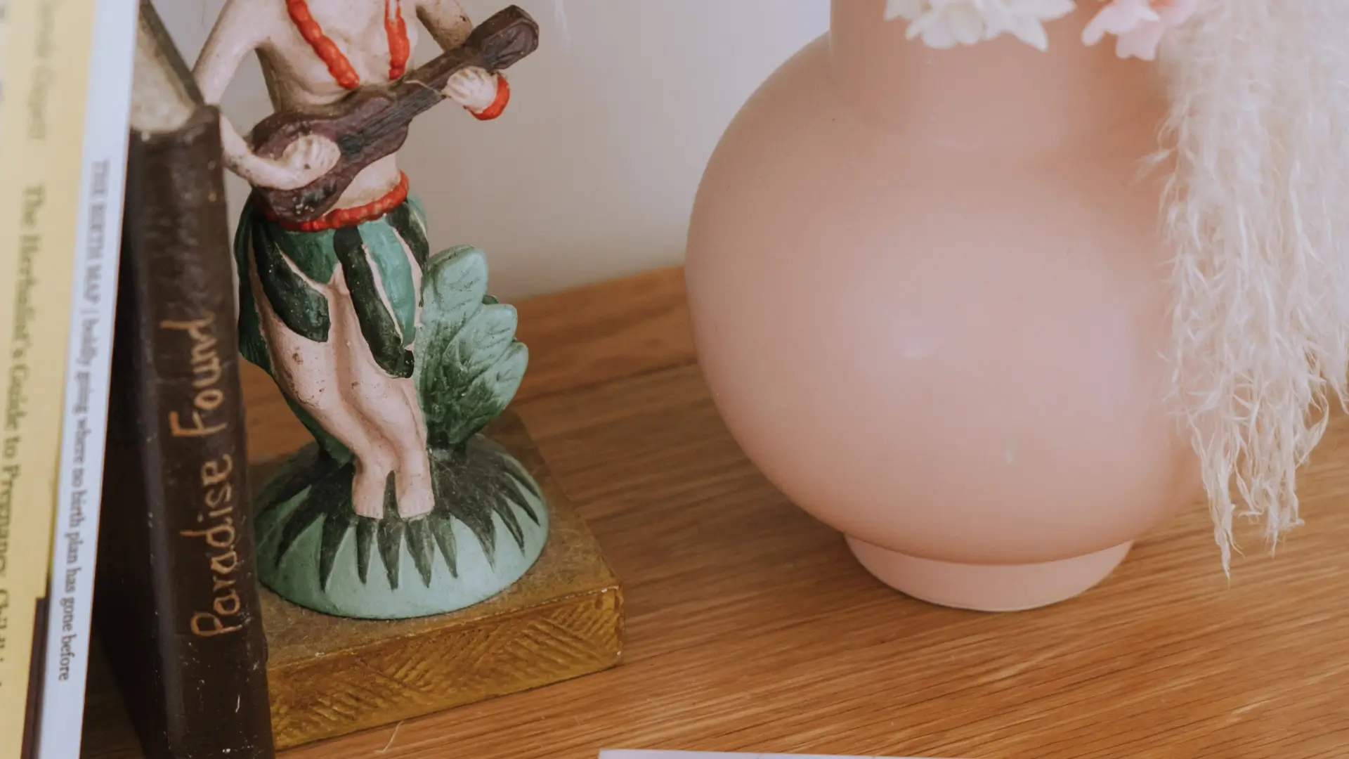 Close-up shot of a clay figuring playing guitar, beside a pink circular vase and books