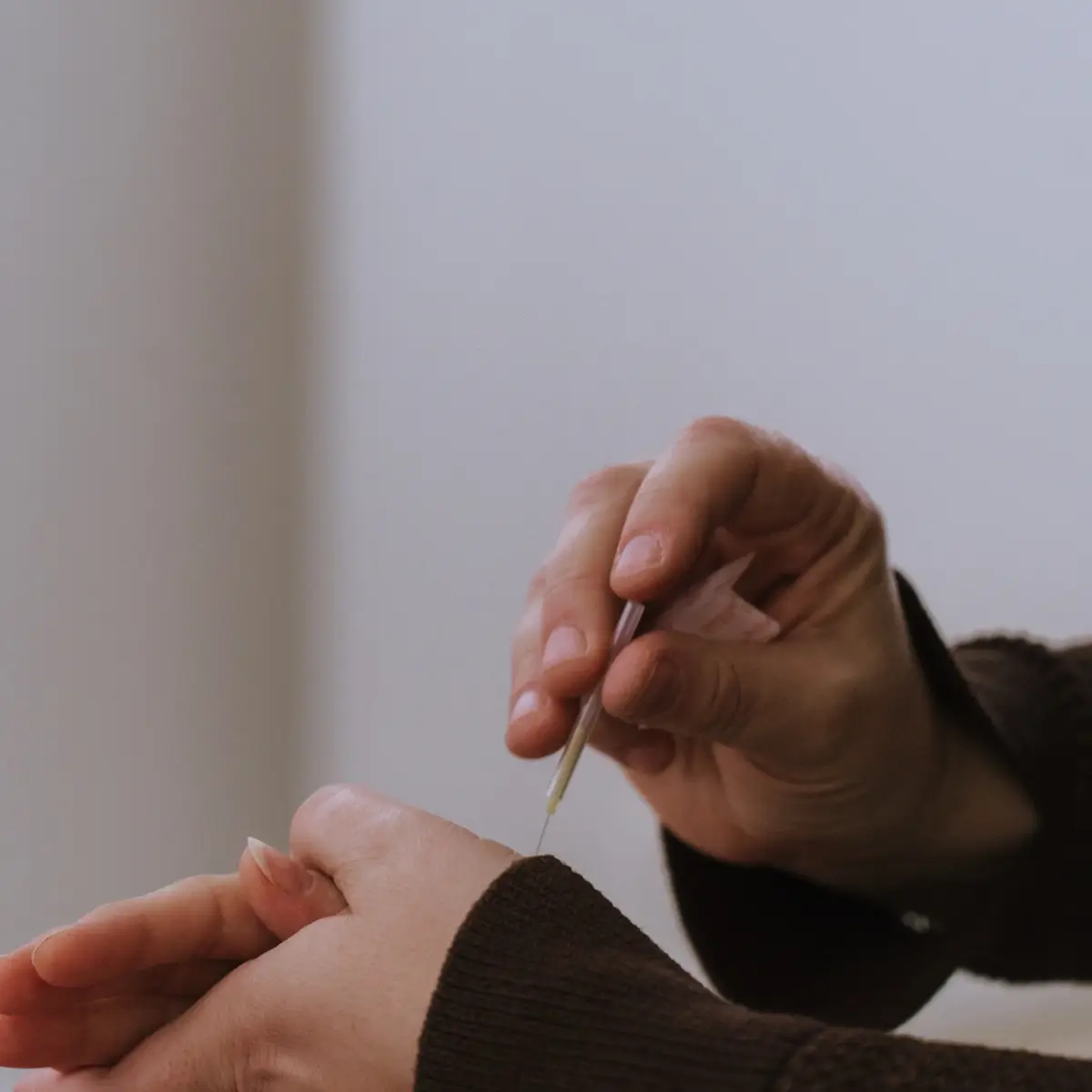 Photo of a midwife's hands performing acuneedling on a client's hand during a prenatal session