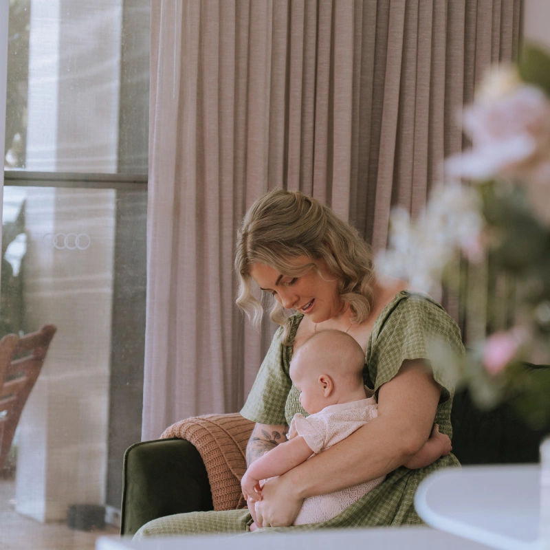 Photo of Caitlin smiling while holding a baby during a postnatal home visit