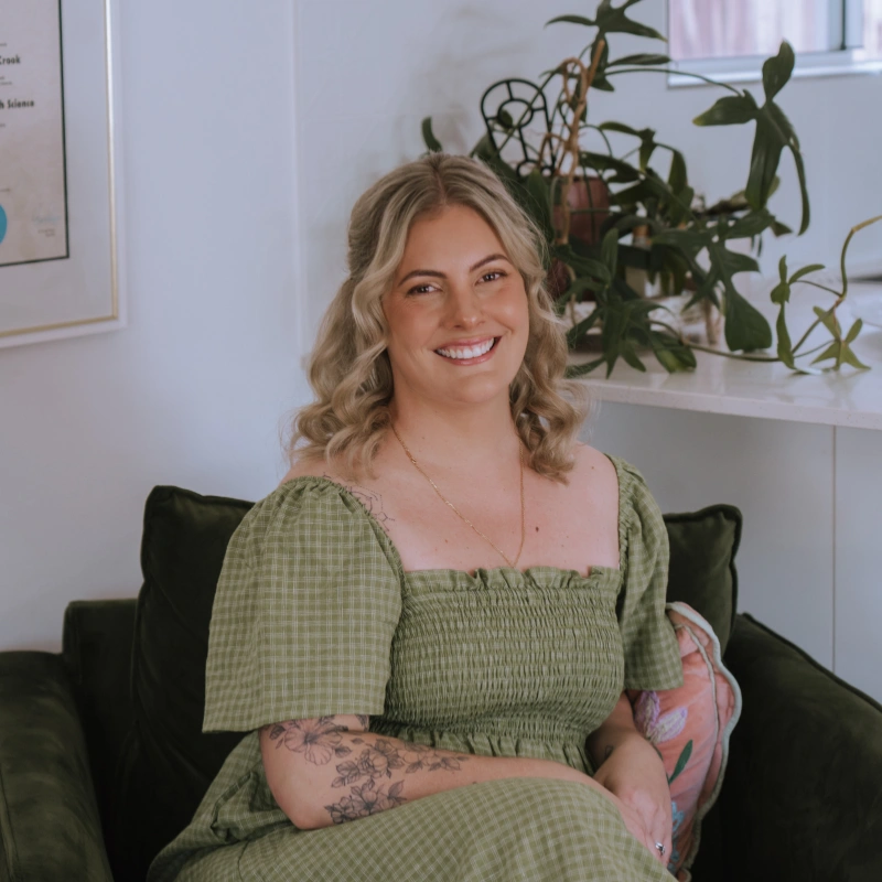 Half body shot of Caitlin smiling while sitting on a green couch