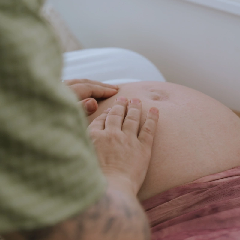 Photo of a midwife's hands gently palpating a pregnant woman's belly during a prenatal appointment