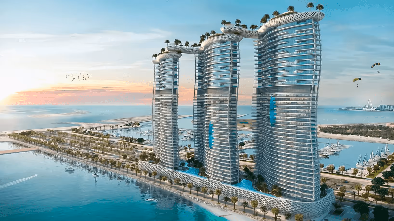 Three modern curved glass towers interconnected by elevated sky bridges with palm trees, overlooking a marina and waterfront at sunset.