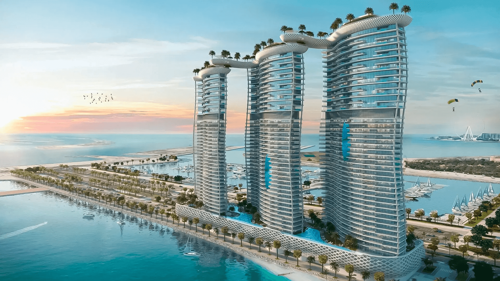 Three modern curved glass towers interconnected by elevated sky bridges with palm trees, overlooking a marina and waterfront at sunset.
