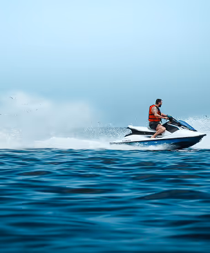 Man wearing a red life jacket riding a jet ski on the ocean with splashing water.