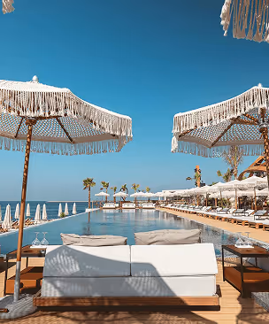 Luxury poolside seating area with white umbrellas overlooking a calm ocean under a clear blue sky.