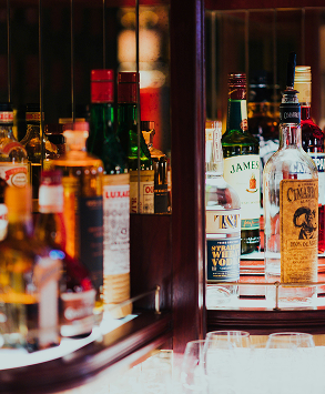 Various liquor bottles arranged on a mirrored bar shelf, including Jameson and Cimarron whiskey.