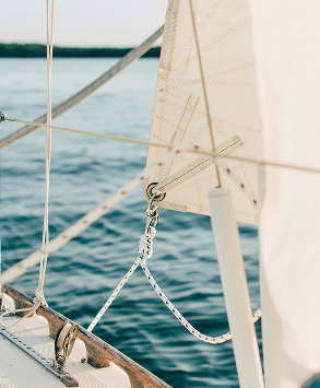 Close-up of sailboat rigging with a white sail against blue water background.