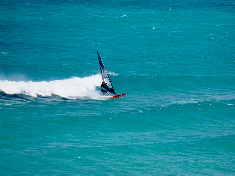 Person windsurfing on a red board over blue ocean waves.