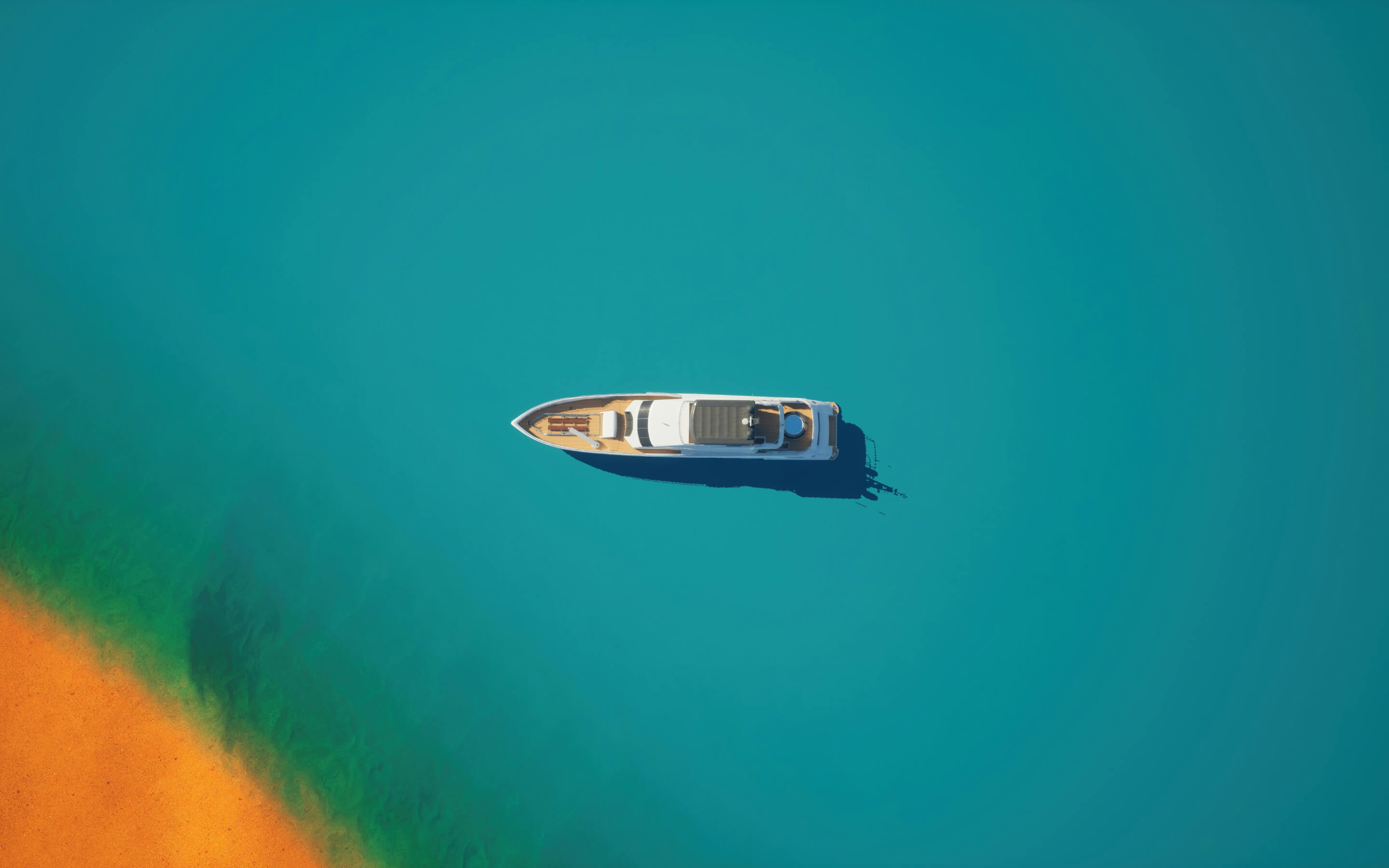 Aerial view of a white yacht floating on clear blue water near a sandy shoreline.