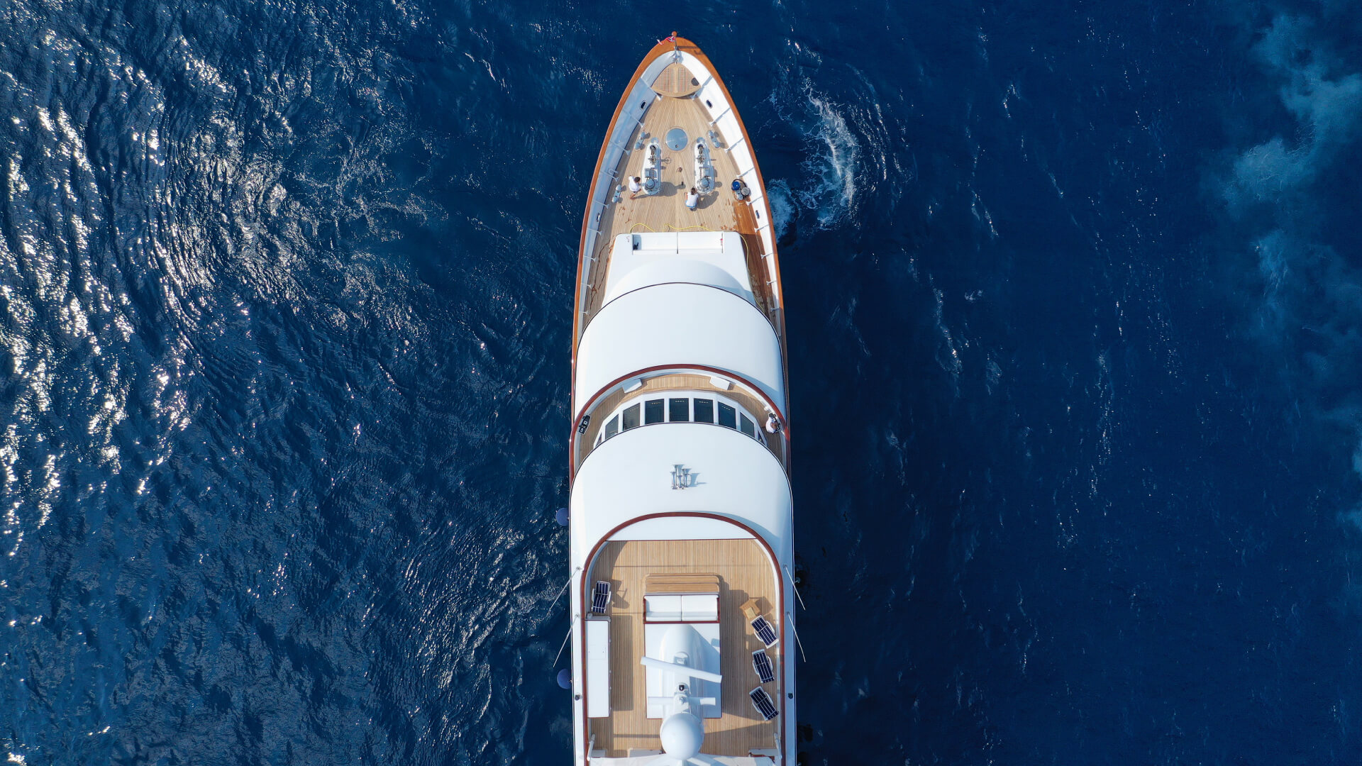 Aerial view of the deck of a white yacht cruising on deep blue water.