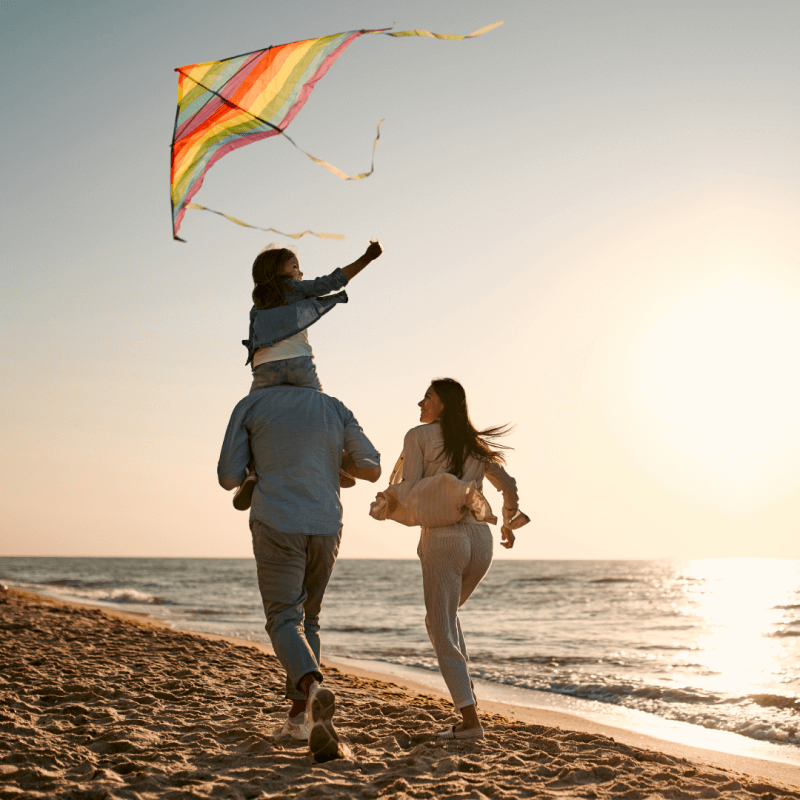 Family running along the beach at sunset with a child flying a colorful kite.