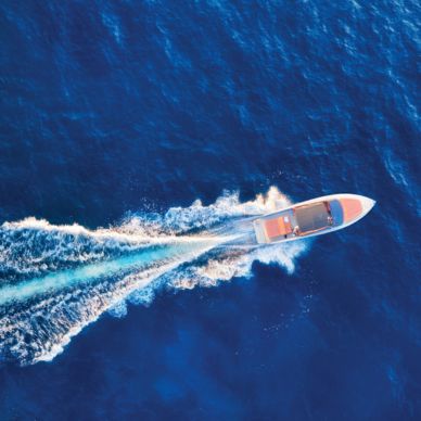 A white motorboat speeding through deep blue water leaving a foamy wake behind.