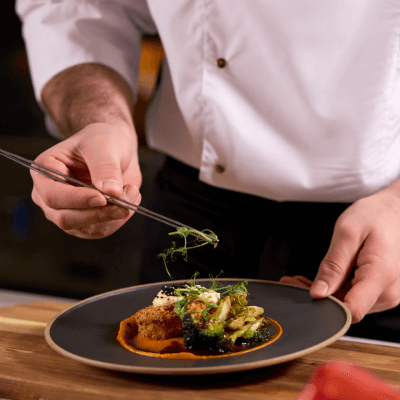 Chef garnishing a gourmet dish on a black plate with tweezers.