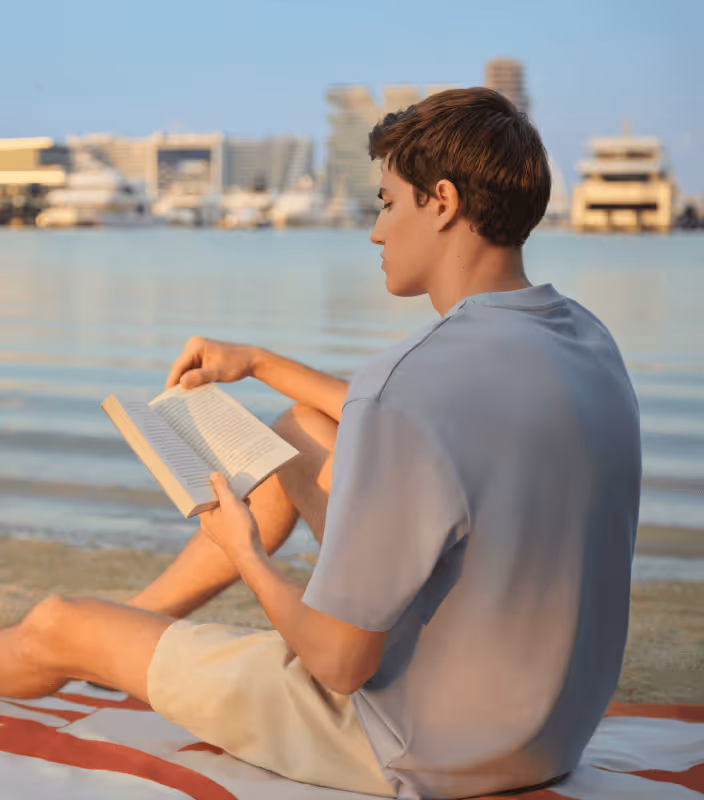 Guy reading book at seafront
