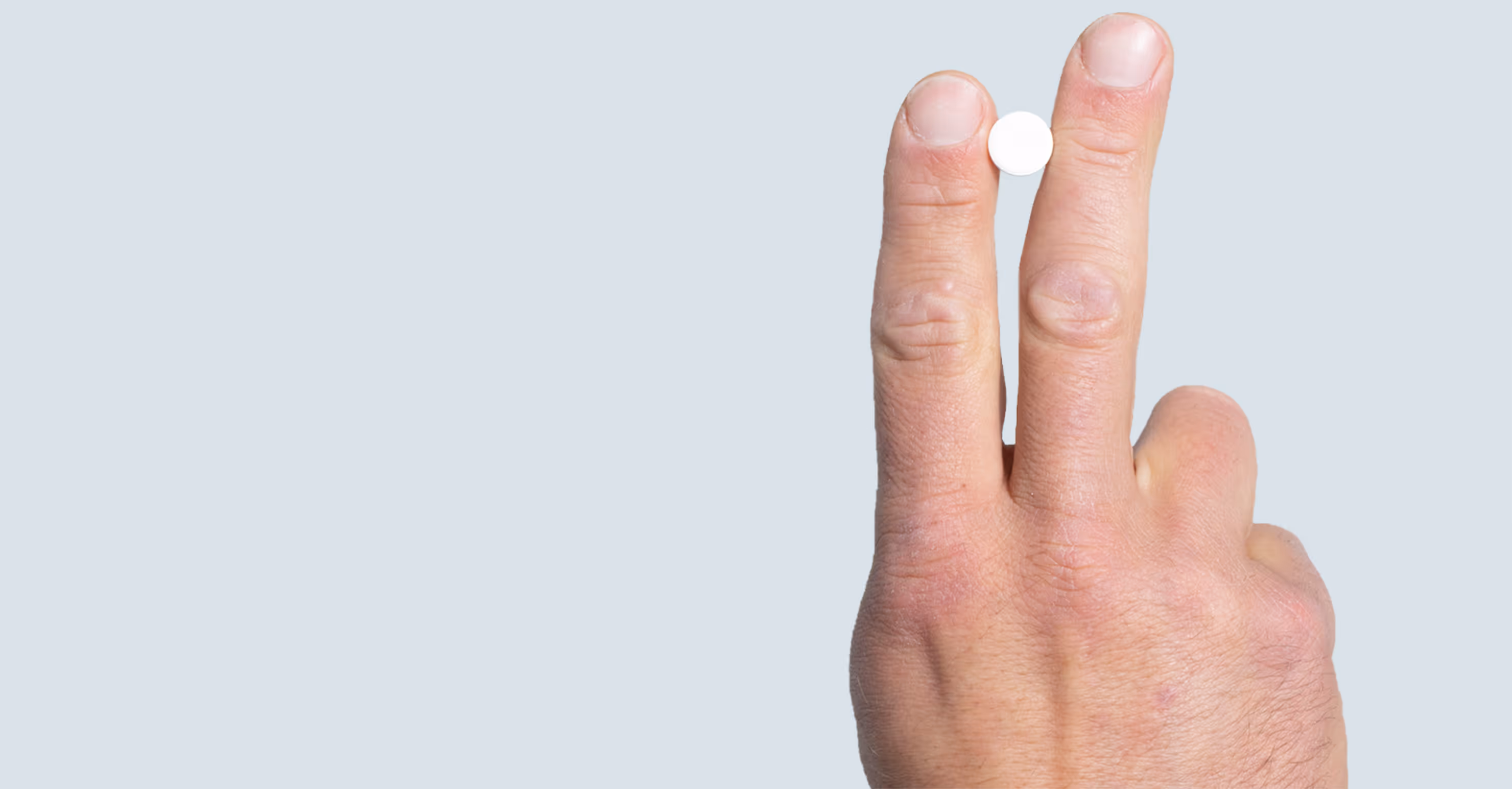 Hand holding a pill between fingers representing ED medications like Cialis and Viagra for erectile dysfunction treatment options