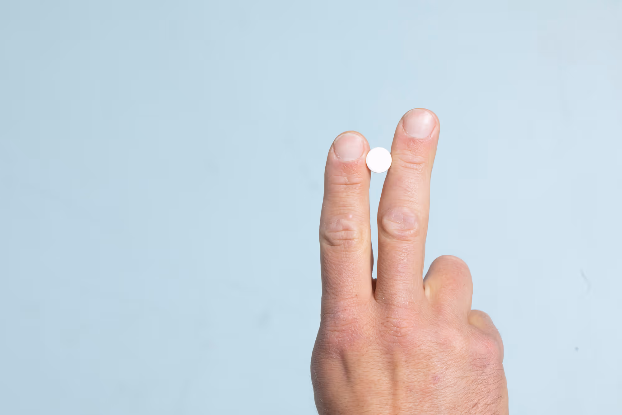 Hand holding a pill between fingers representing generic vs brand-name Viagra options for erectile dysfunction treatment in men