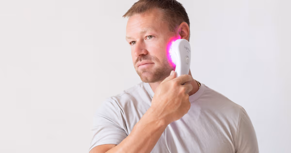 Man using handheld red light therapy device on face to improve skin tone, reduce wrinkles, and support collagen production