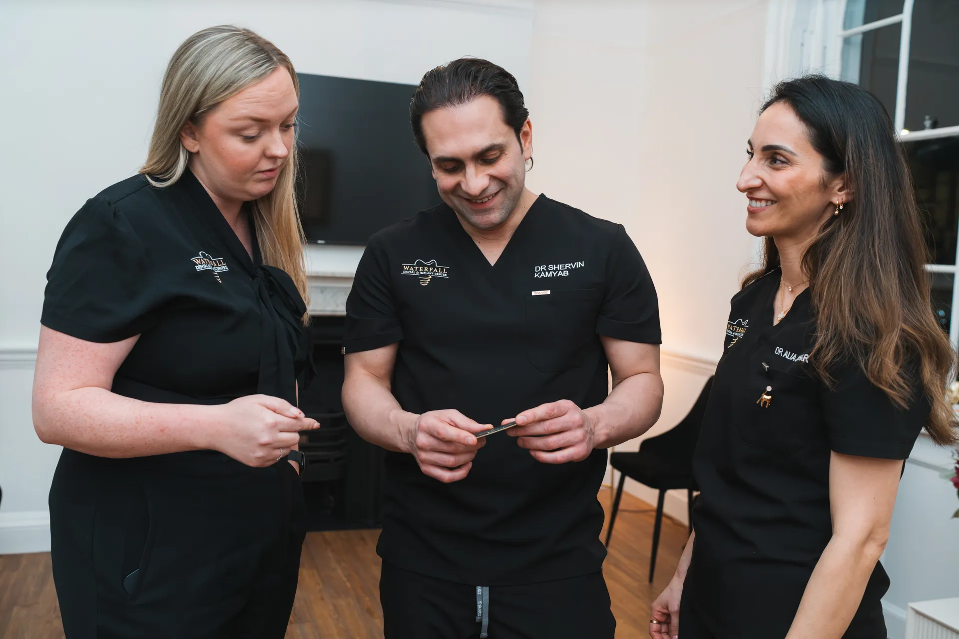 Three dental professionals in black scrubs standing and discussing an item held by the man in the middle.