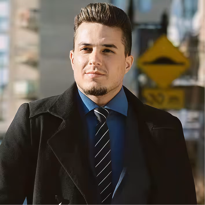 Homme d'affaires portant un manteau noir, chemise bleue et cravate rayée debout en extérieur.