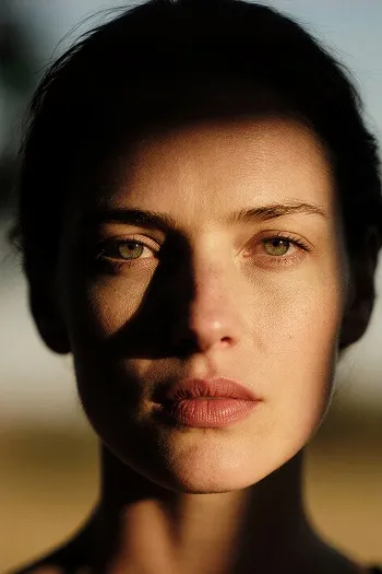 Close-up portrait of a woman with green eyes, half of her face covered in shadow.