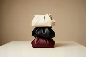 Stack of three folded leather clutch bags in cream, black, and burgundy colors on a white surface against a beige background.
