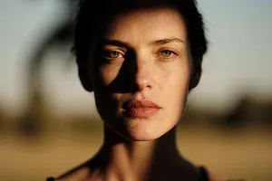 Close-up portrait of a woman with light and shadow on her face against an outdoor blurred background.