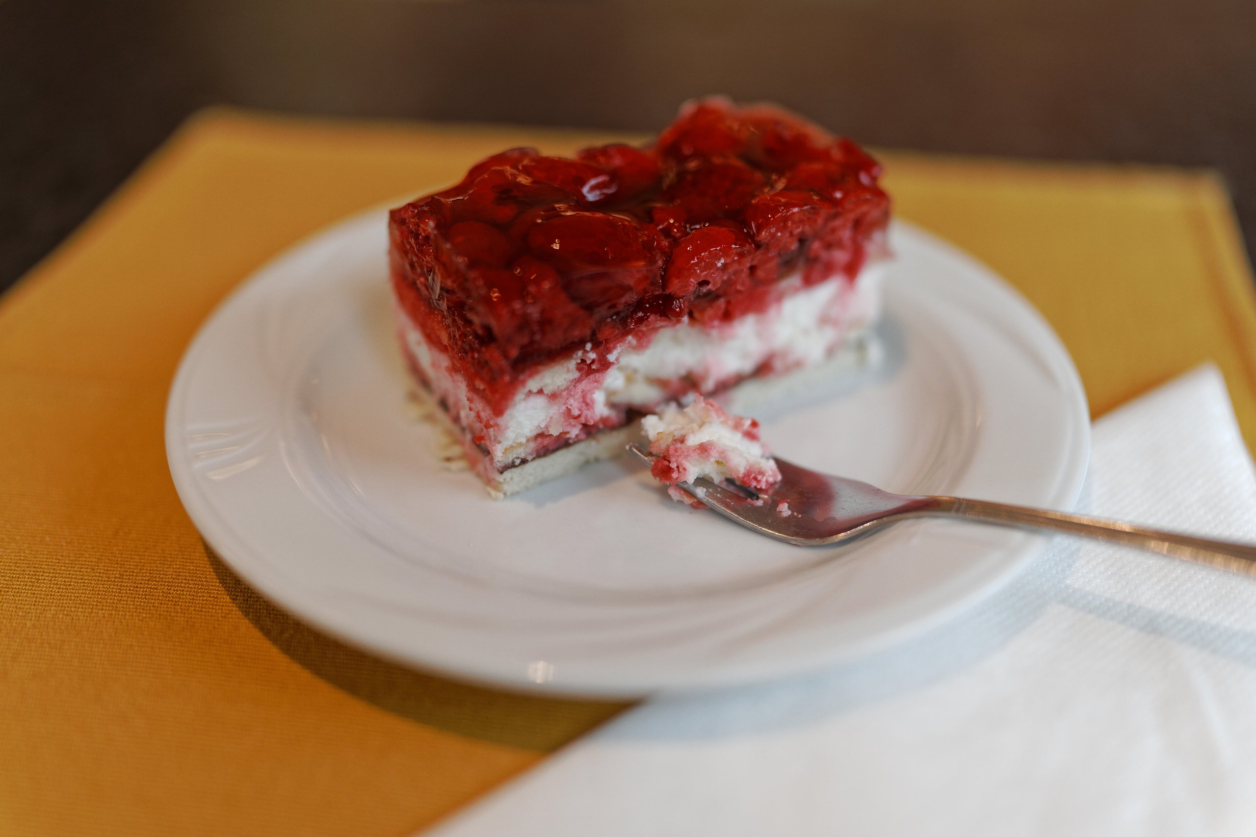 Slice of layered strawberry dessert with cream on a white plate with a fork holding a bite.
