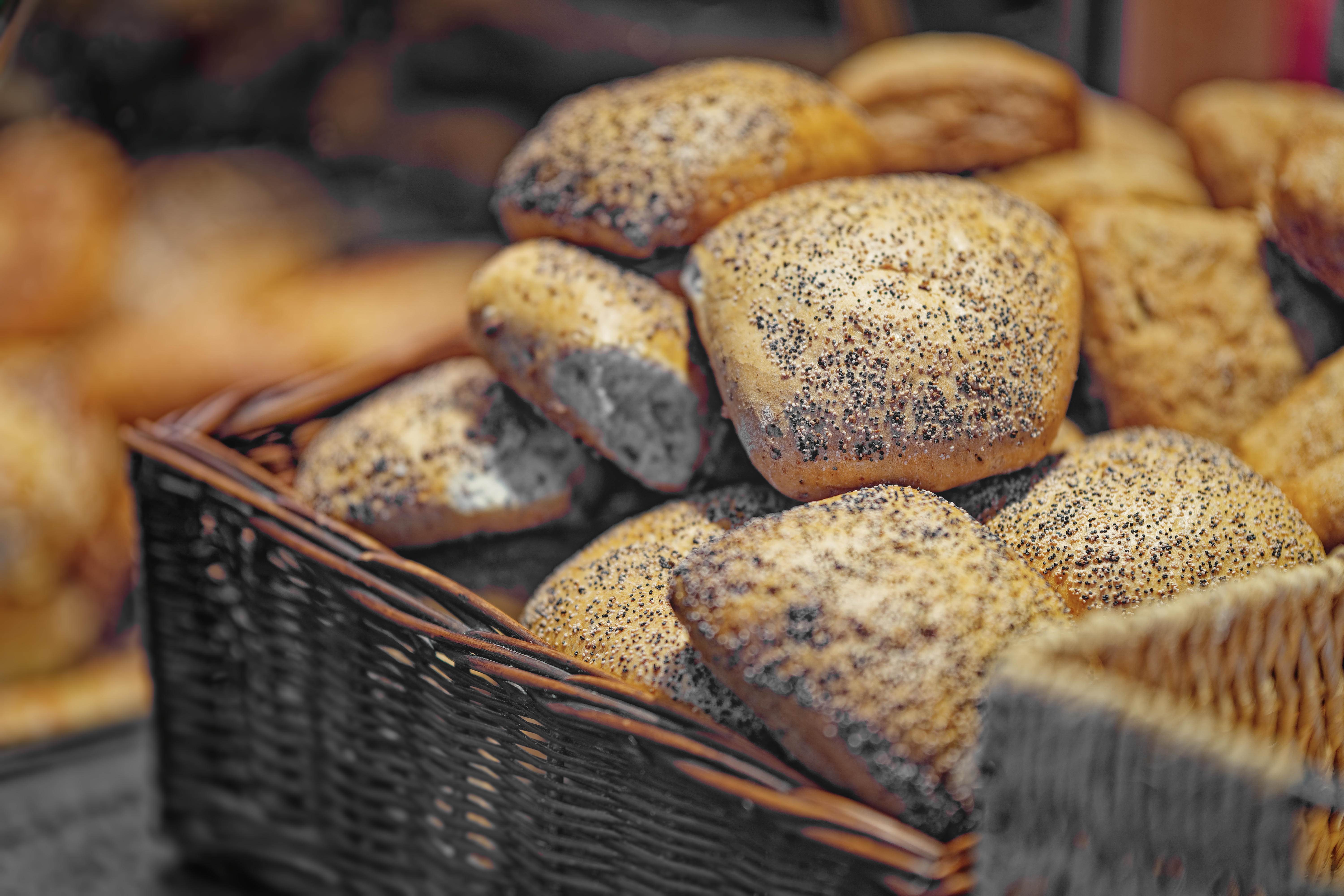 Wicker basket filled with fresh baked bread rolls topped with poppy seeds.