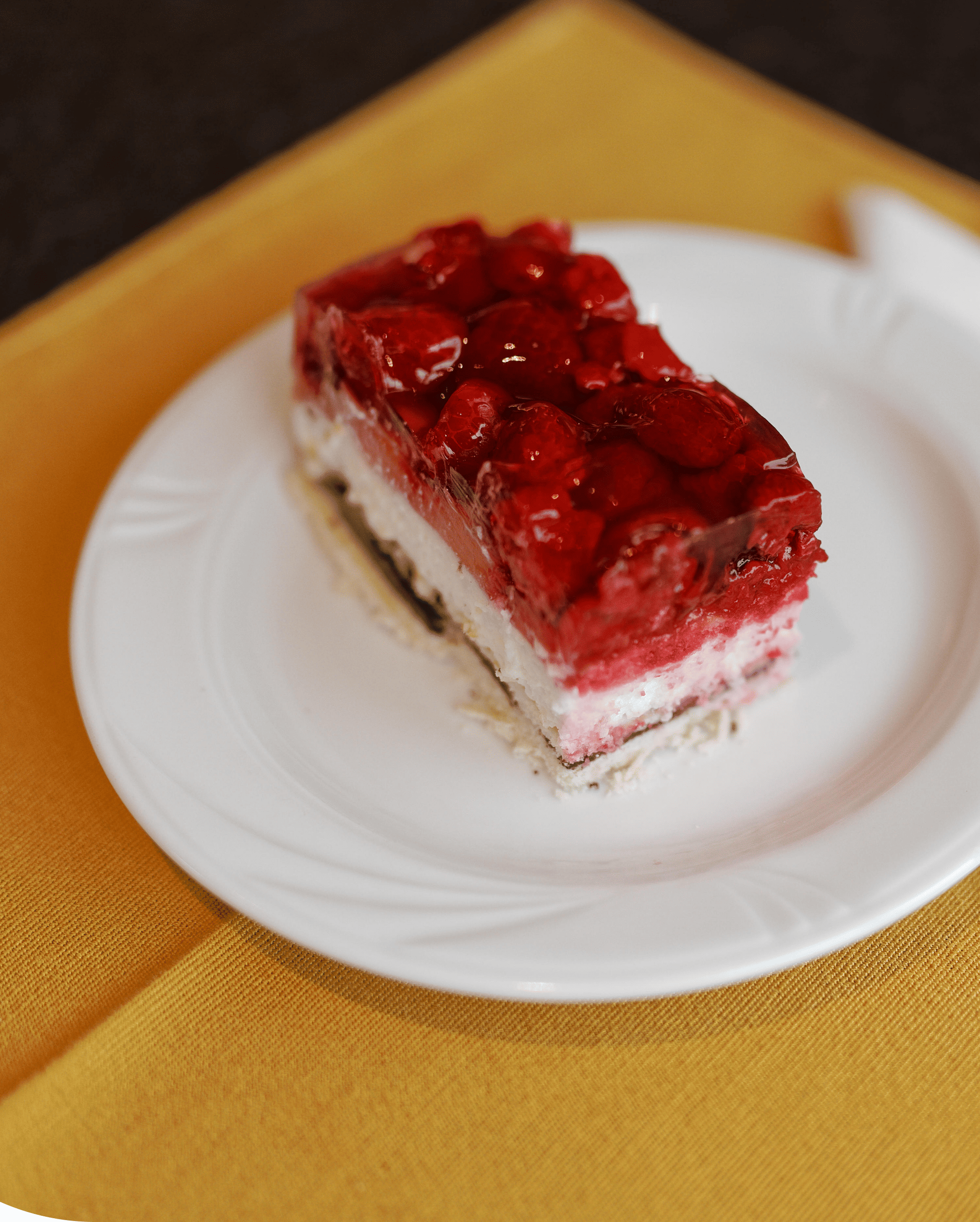Slice of layered strawberry dessert with cream and jelly on a white plate over a yellow cloth.