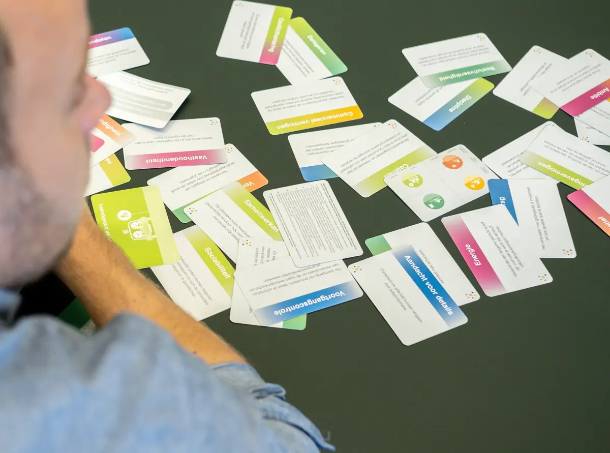Man in blue shirt looking at scattered, colorful text cards on a dark green table.